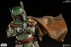 Boba Fett sixth-scale figure aiming a blaster rifle, wearing chipped green armor and a brown cape stretched across the black background