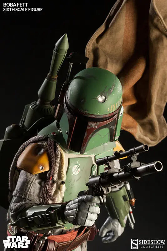 Close-up of the Boba Fett sixth-scale figure holding a blaster rifle, with a green jetpack, chipped helmet, yellow shoulder armor, and brown cape behind him