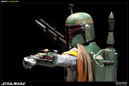 Boba Fett sixth-scale figure in green and red weathered armor, aiming a wrist-mounted gauntlet weapon with a blaster rifle and jetpack visible against a black background.