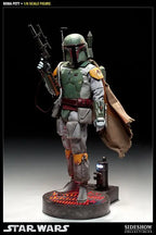 Full-body Boba Fett sixth-scale figure standing on a display base with a blaster rifle, jetpack, brown cape, and weathered green armor