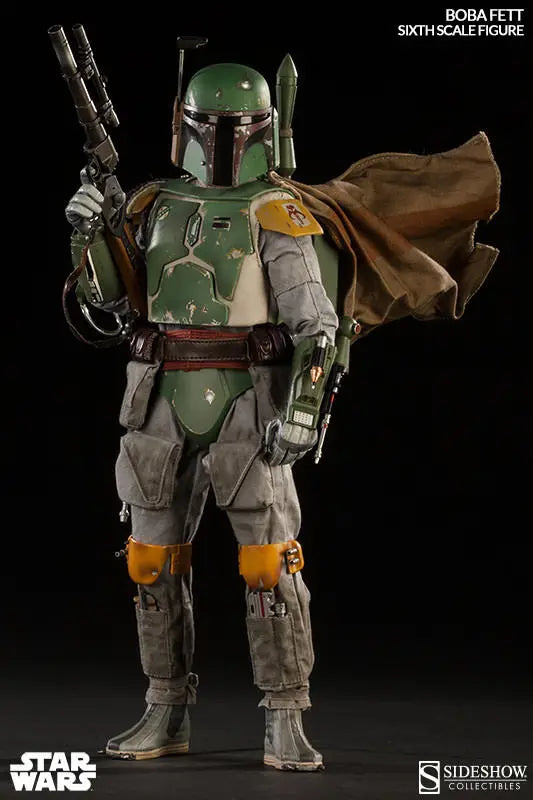 Front view of the Boba Fett sixth-scale figure holding a blaster rifle, with chipped green armor, yellow knee pads, gray flight suit, brown utility belt, jetpack, and cape